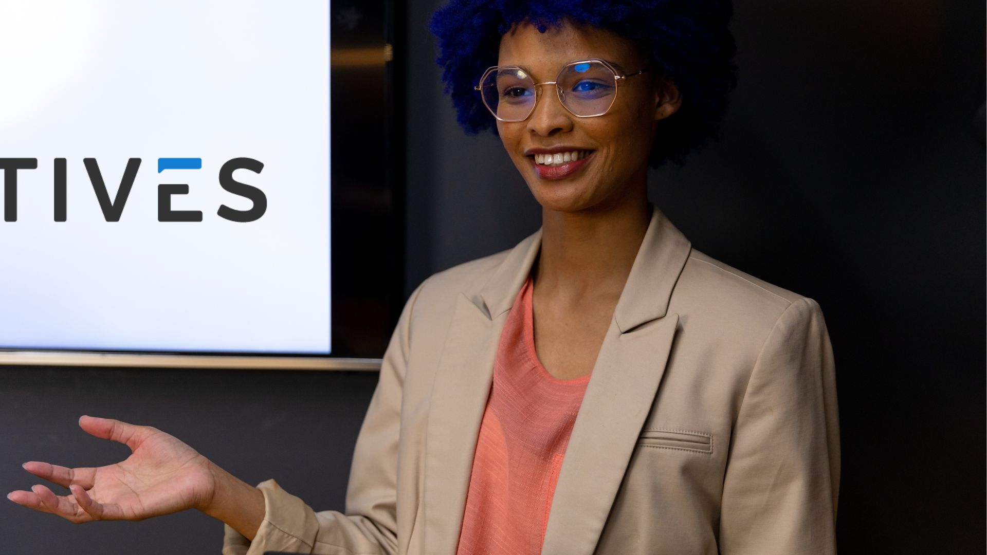 A confident professional with blue hair and glasses presents in front of a screen displaying the Electives logo. This image reflects the enthusiasm and engagement encouraged in the blog post about launching a small-budget L&D program. The presenter's demeanor emphasizes the importance of leadership and manager involvement in promoting and participating in learning opportunities within the organization.