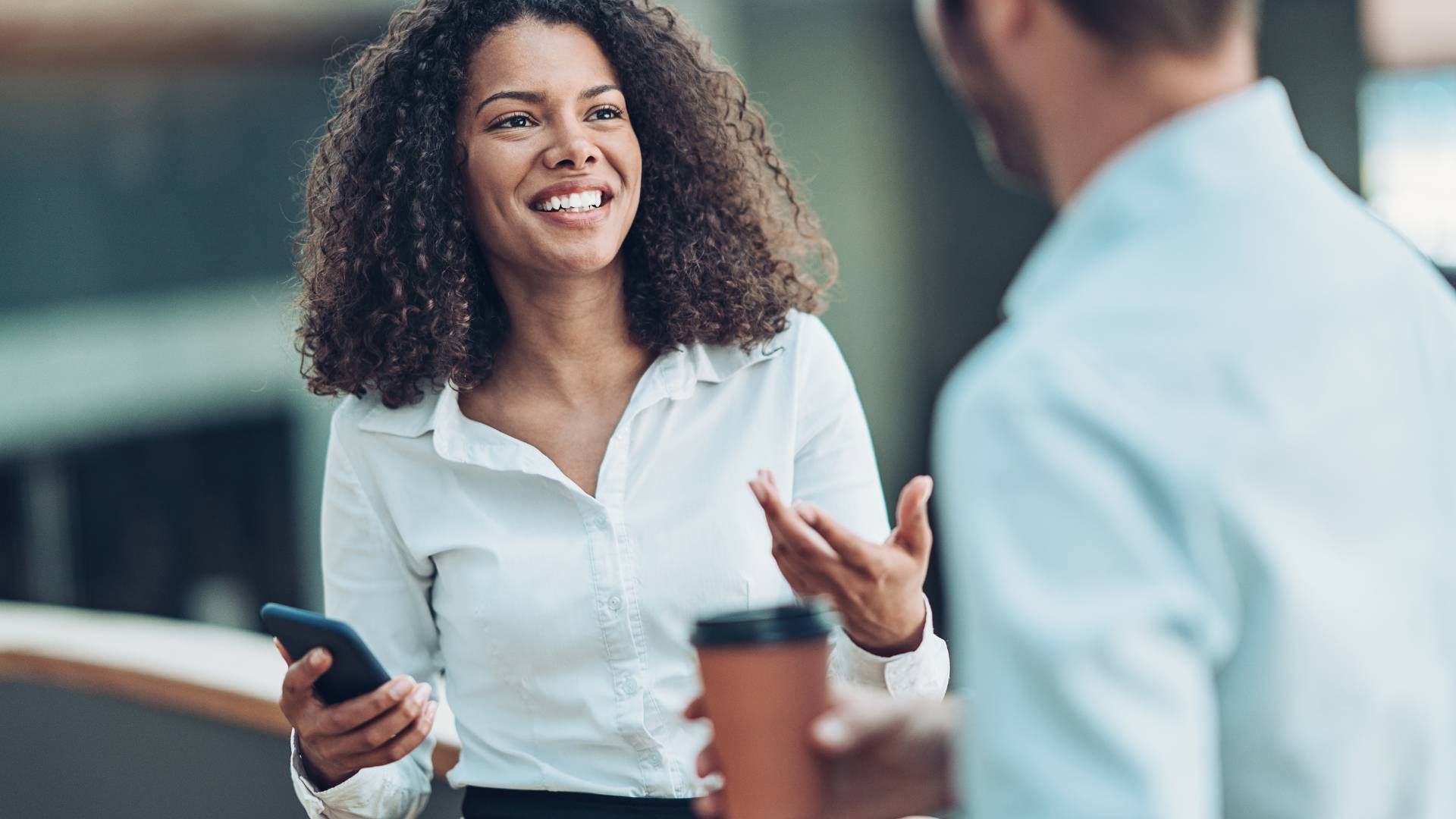 We are looking over a man's shoulder at a smiling woman who is talking to him.