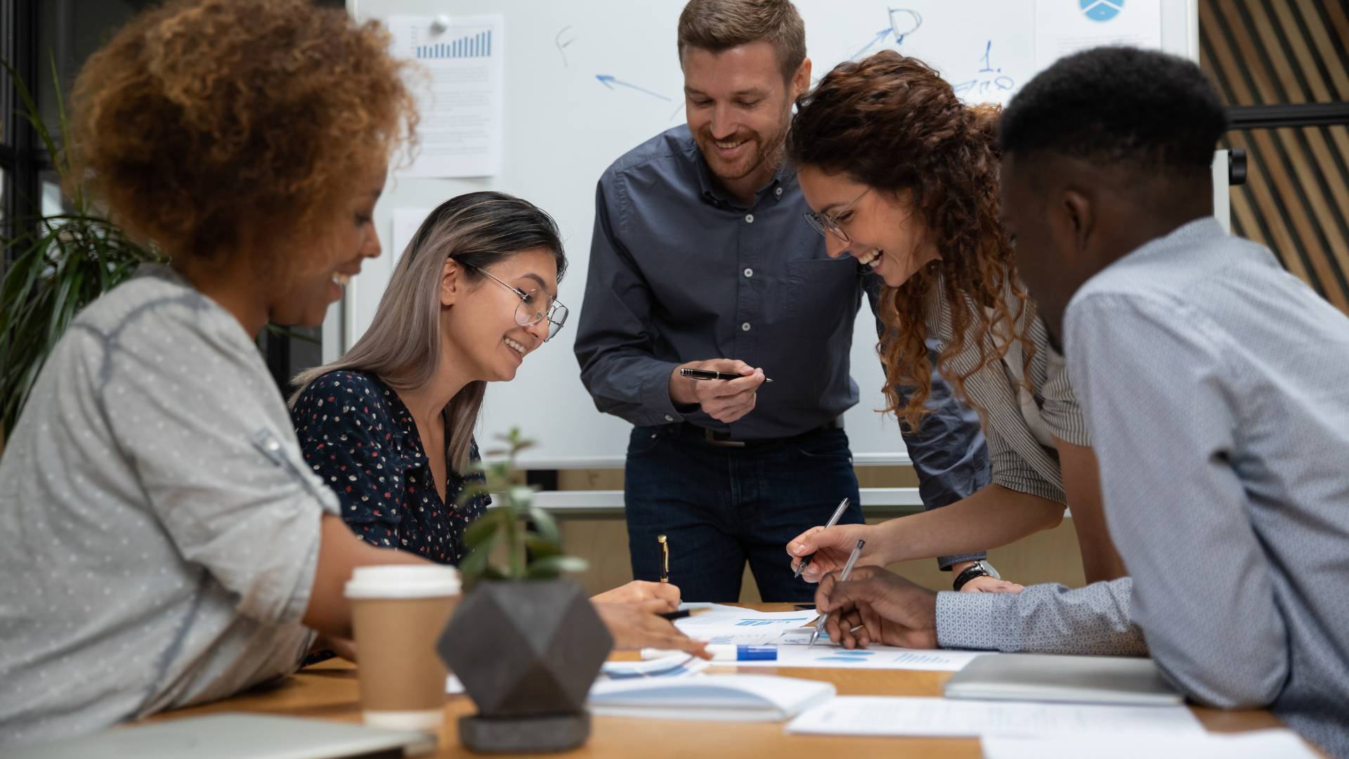There are employees gathered around a conference table having a meeting. They're laughing and smiling.