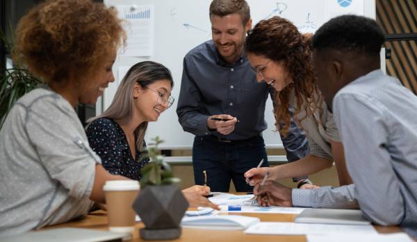 There are employees gathered around a conference table having a meeting. They're laughing and smiling.