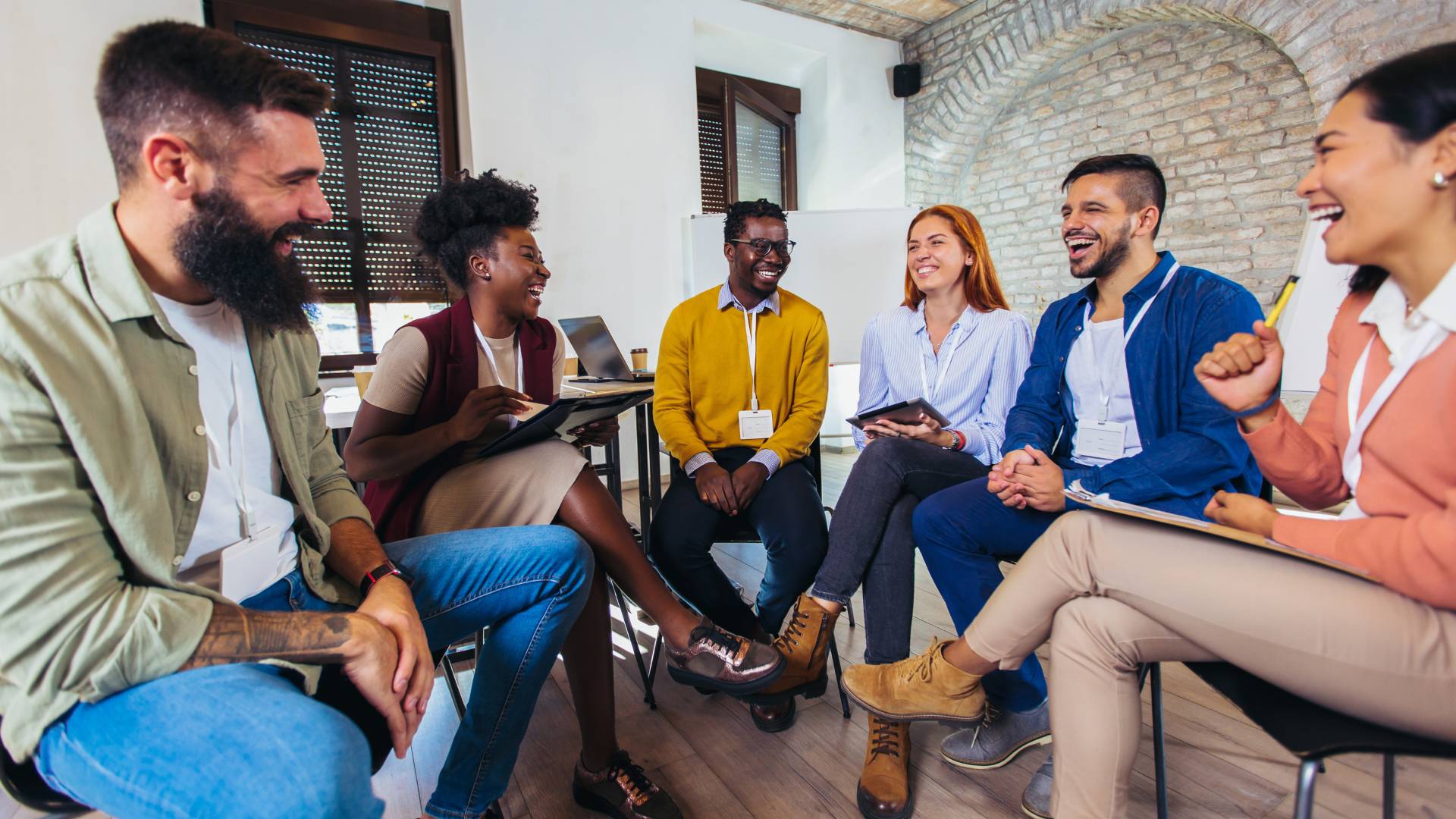 There are six people sitting around in a circle in an office. They are laughing and smiling.
