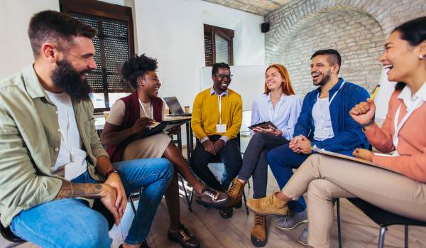There are six people sitting around in a circle in an office. They are laughing and smiling.