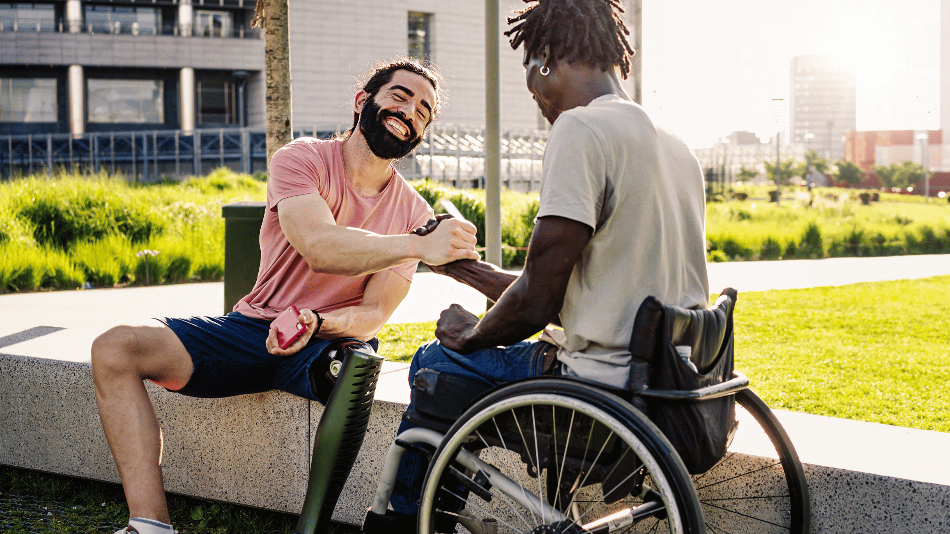 A man with a prosthetic leg and a man in a wheelchair are shaking hands.