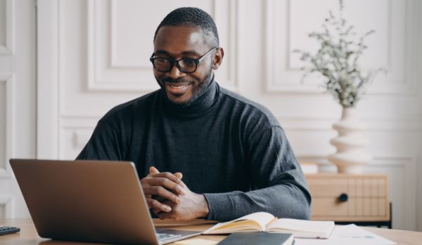 A happy remote worker is smiling down at his laptop.