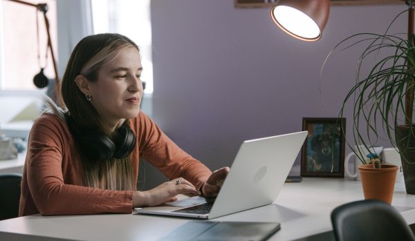 A young, female-presenting professional is working on their laptop at their desk in the office.
