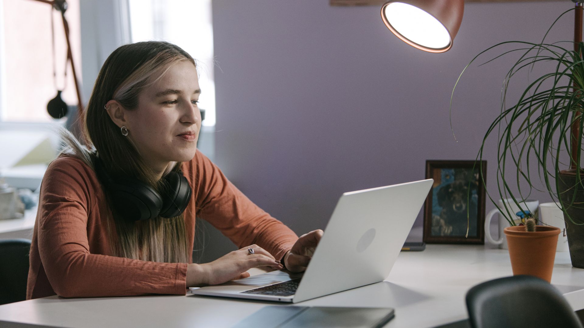 A young, female-presenting professional is working on their laptop at their desk in the office.