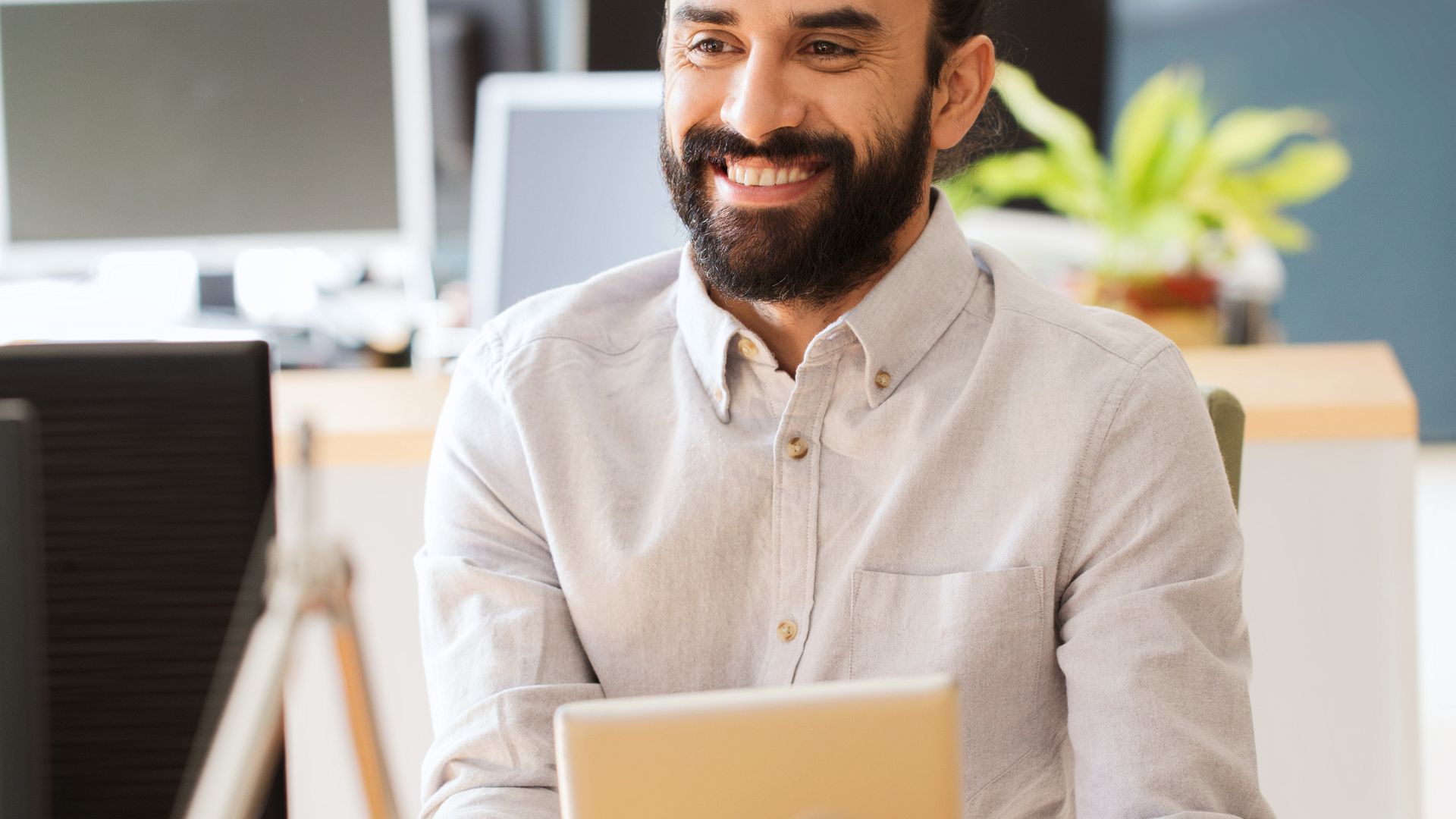 A man is smiling and holding a tablet while seated at a table.