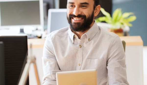 A man is smiling and holding a tablet while seated at a table.