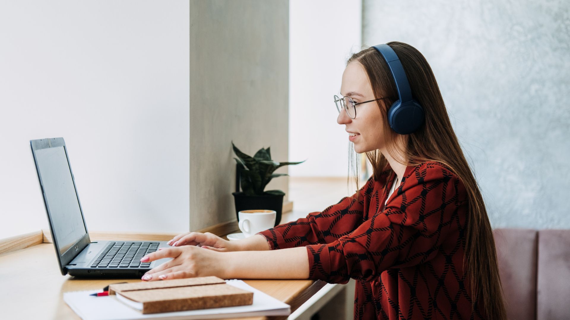 A young woman is participating remotely in a professional development program. She is sitting in front of her laptop with headphones on.