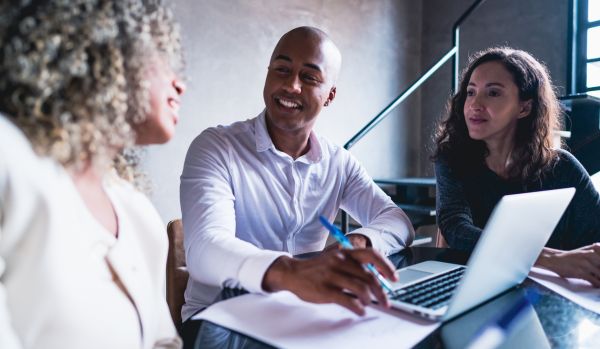 A diverse group of 3 people are working around a laptop in an office.