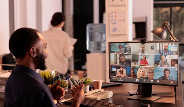 We're looking over the should of a man participating in a virtual training at his monitor with other participants on the screen.