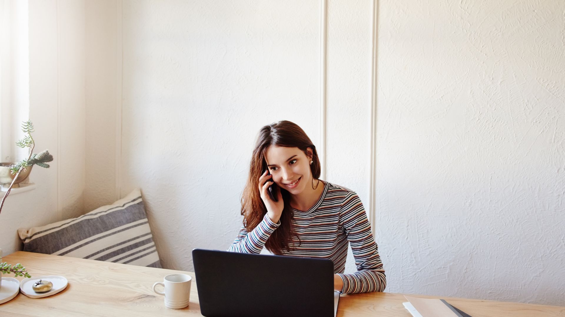 A woman is working from home on her laptop while on her mobile phone.