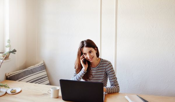 A woman is working from home on her laptop while on her mobile phone.