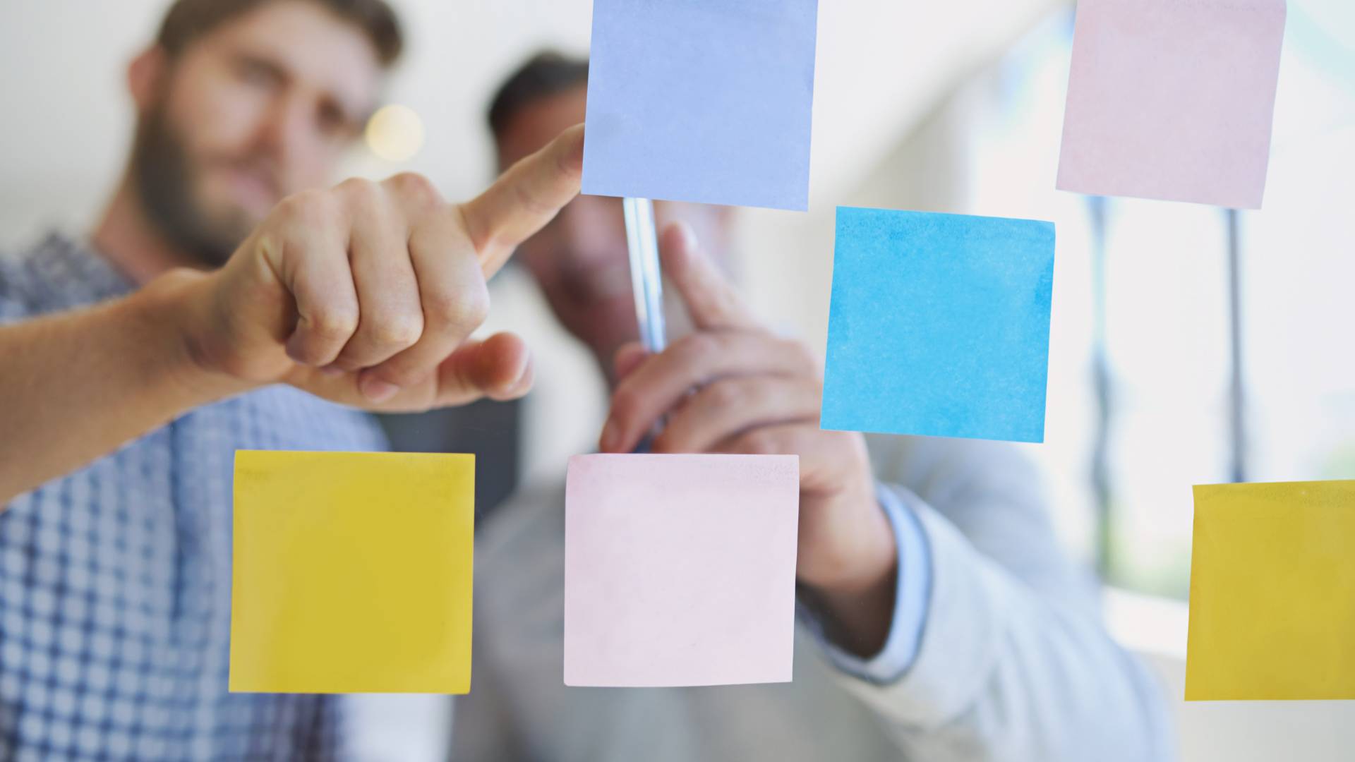 We're looking through a clear whiteboard at two people discussing a series of post-it notes as part of their design thinking process.