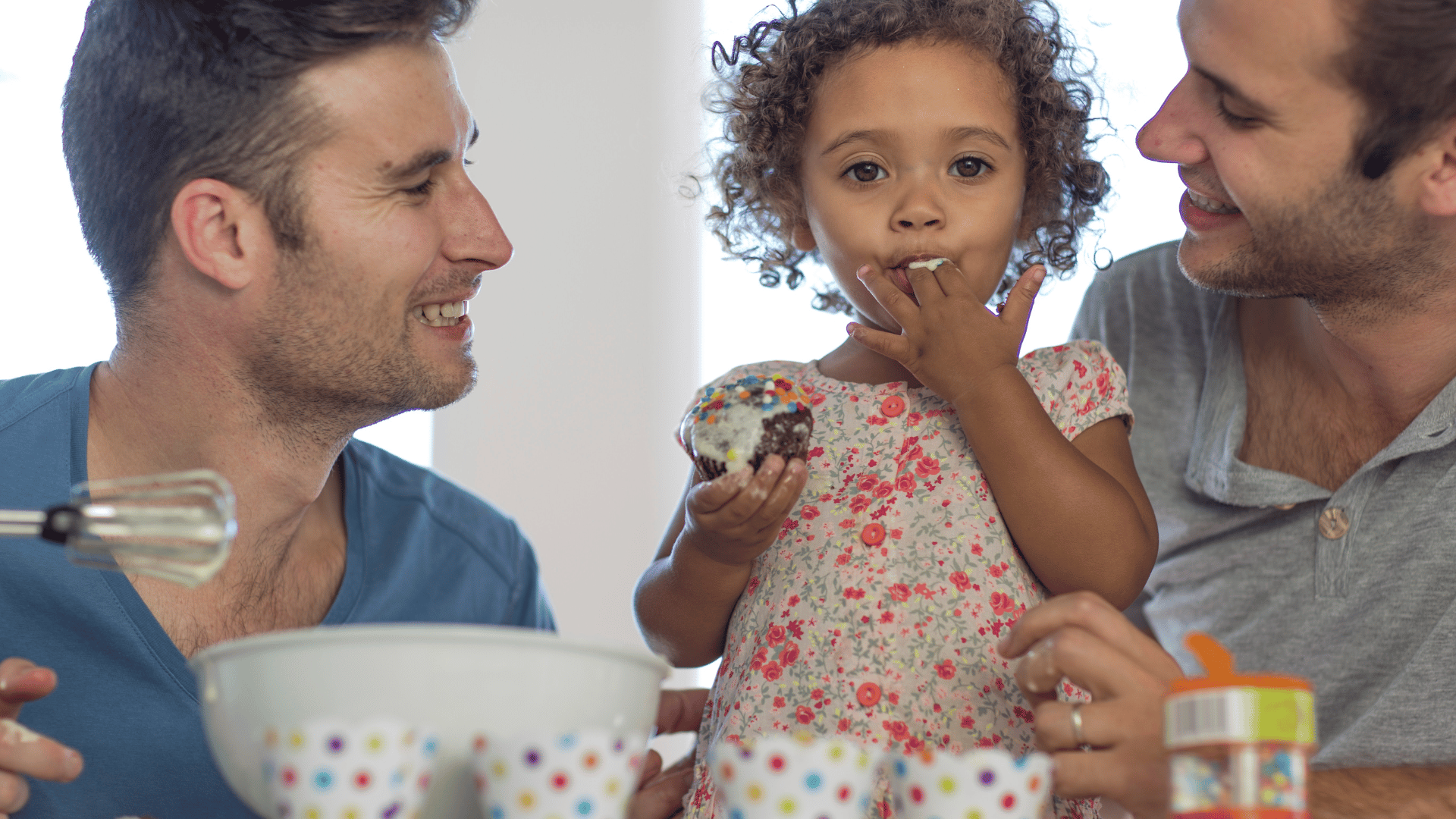A gay male couple with their daughter are baking together.