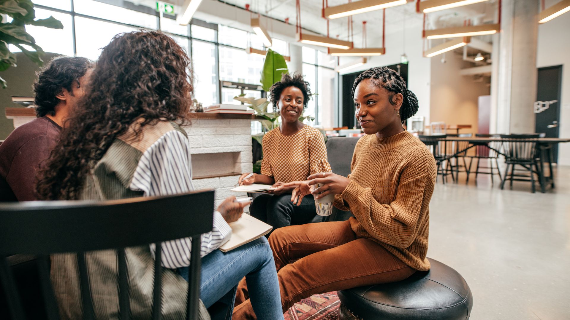 A diverse team of young workers are sitting in an open common area conversing.