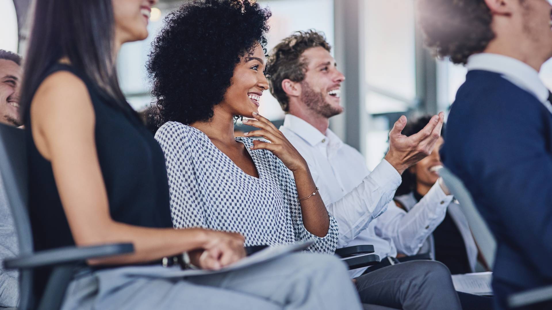 A diverse row of seated training participants in an office are smiling an laughing