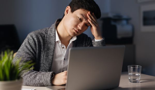 A man is sitting at his laptop with his head in his hands.