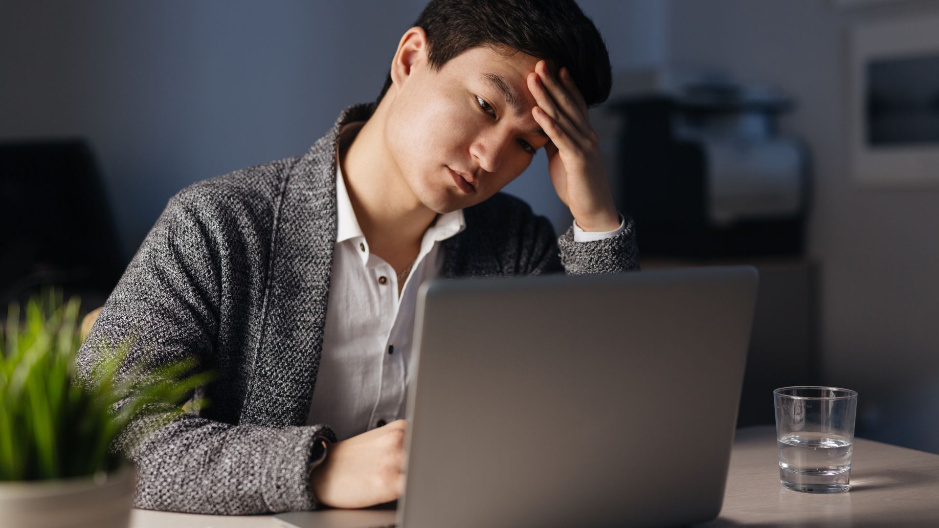 A man is sitting at his laptop with his head in his hands.