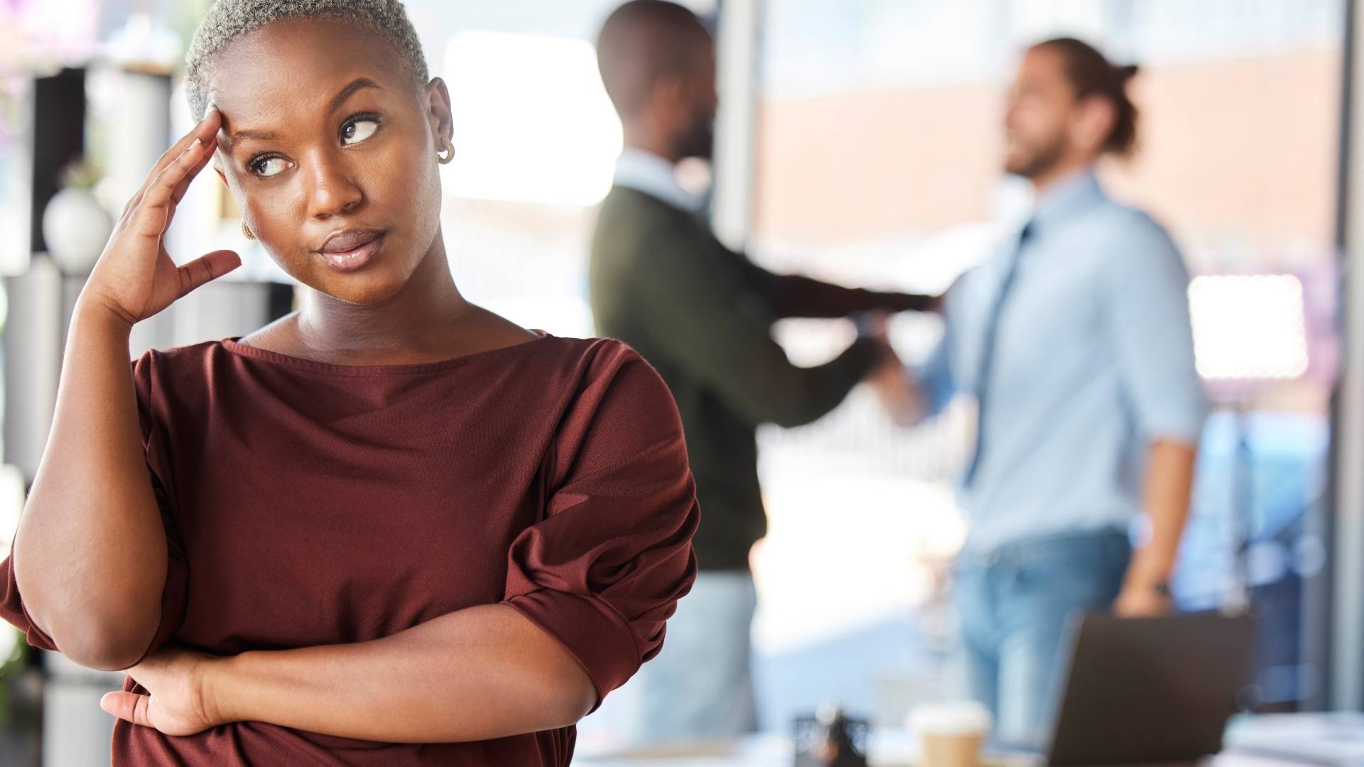 A woman is stressed in the foreground and in the background there are two men conversing.