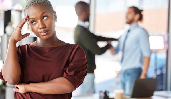 A woman is stressed in the foreground and in the background there are two men conversing.