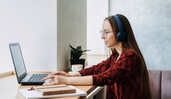 A young professional woman sits at a counter working on her laptop wearing headphones.