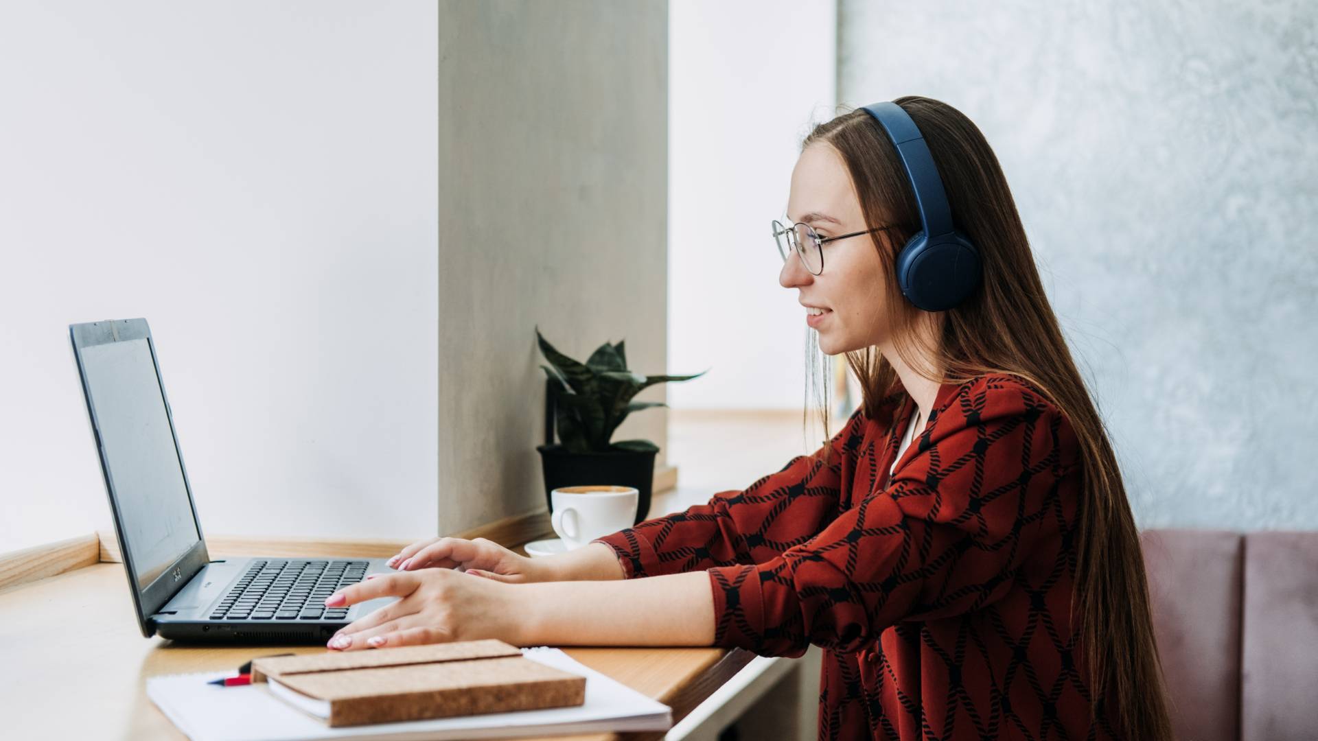 A young professional woman sits at a counter working on her laptop wearing headphones.