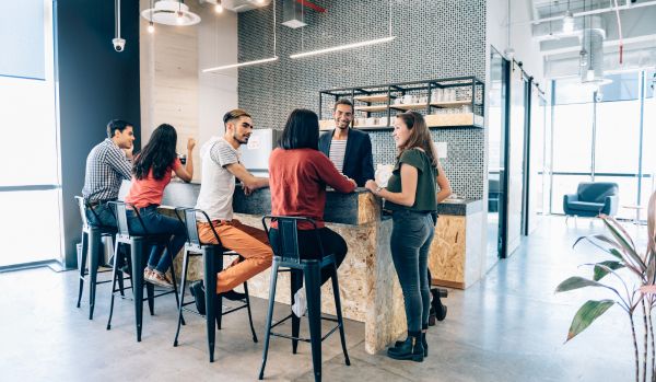 A diverse group of employees is hanging out in the open concept kitchen of their office.