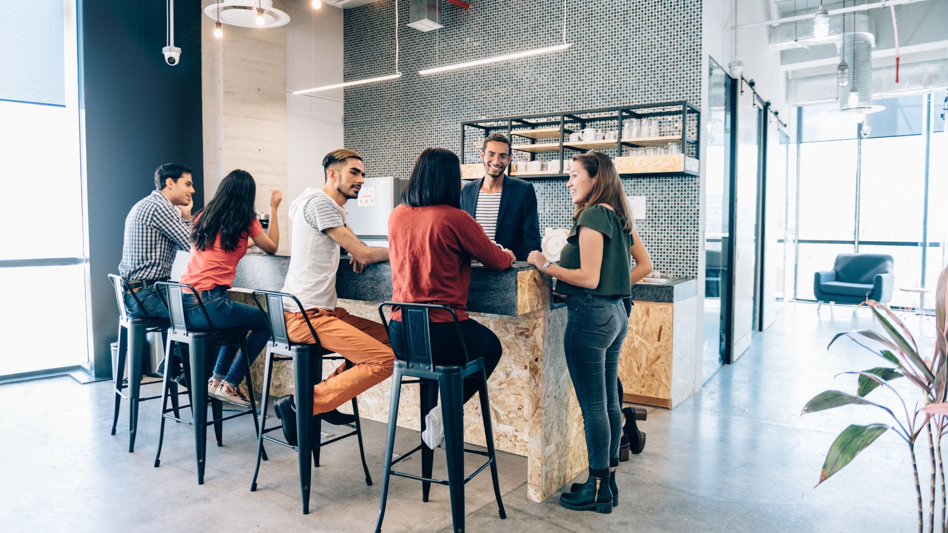 A diverse group of employees is hanging out in the open concept kitchen of their office.