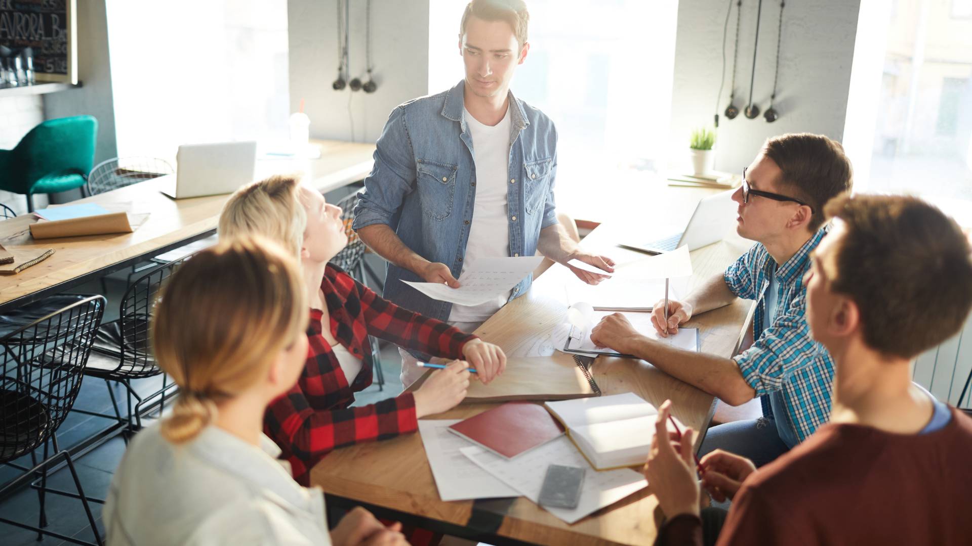 A group of workers are in an office gathered around a table brainstorming ideas. There are five people in total.