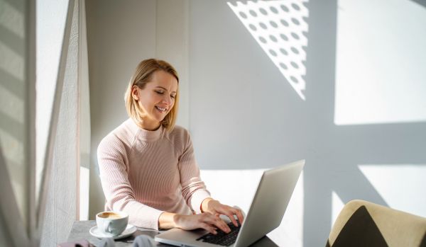 A woman is using AI on her laptop in a coffee shop.