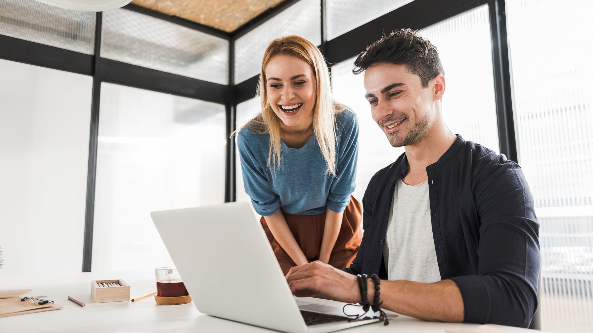 Two coworkers are smiling as they compare learning tools on one of their laptops.