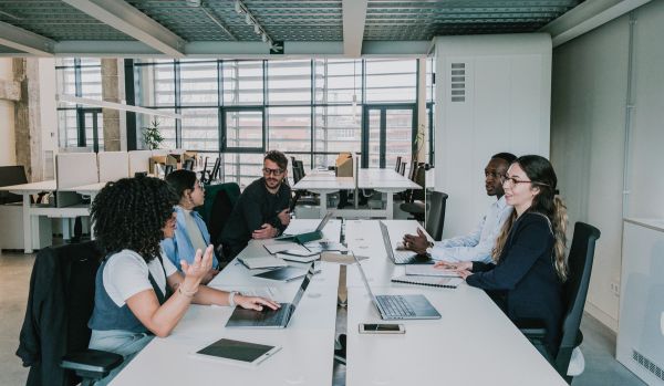 A diverse team of people are sitting around a conference table with their laptops comparing corporate training providers.