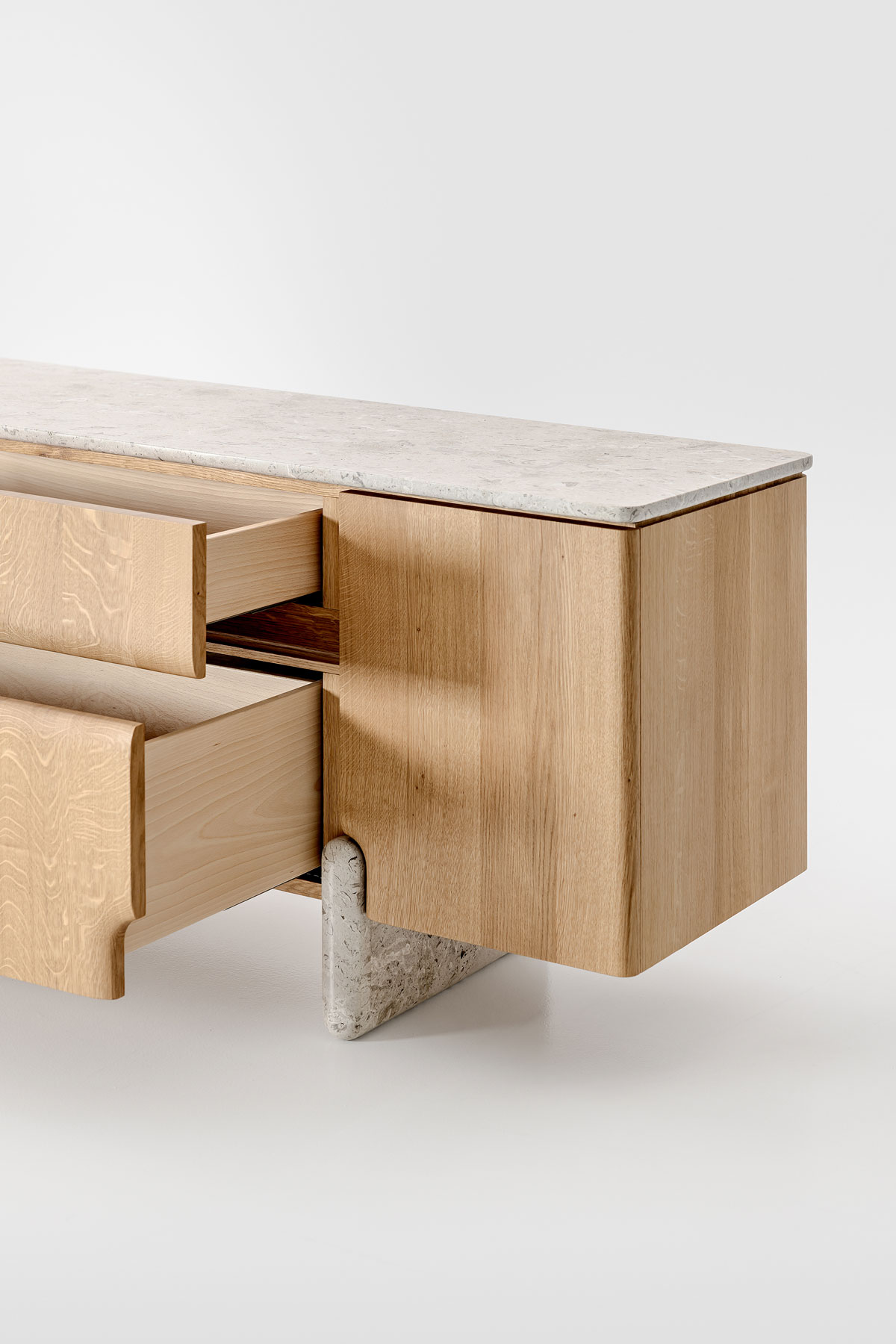 Schrägansicht des Sideboards Onde von formstelle für Zeitraum in Eiche mit Steinfüßen und Marmor Platte und ausgezogenen Schubladen vor hellem Hintergrund.