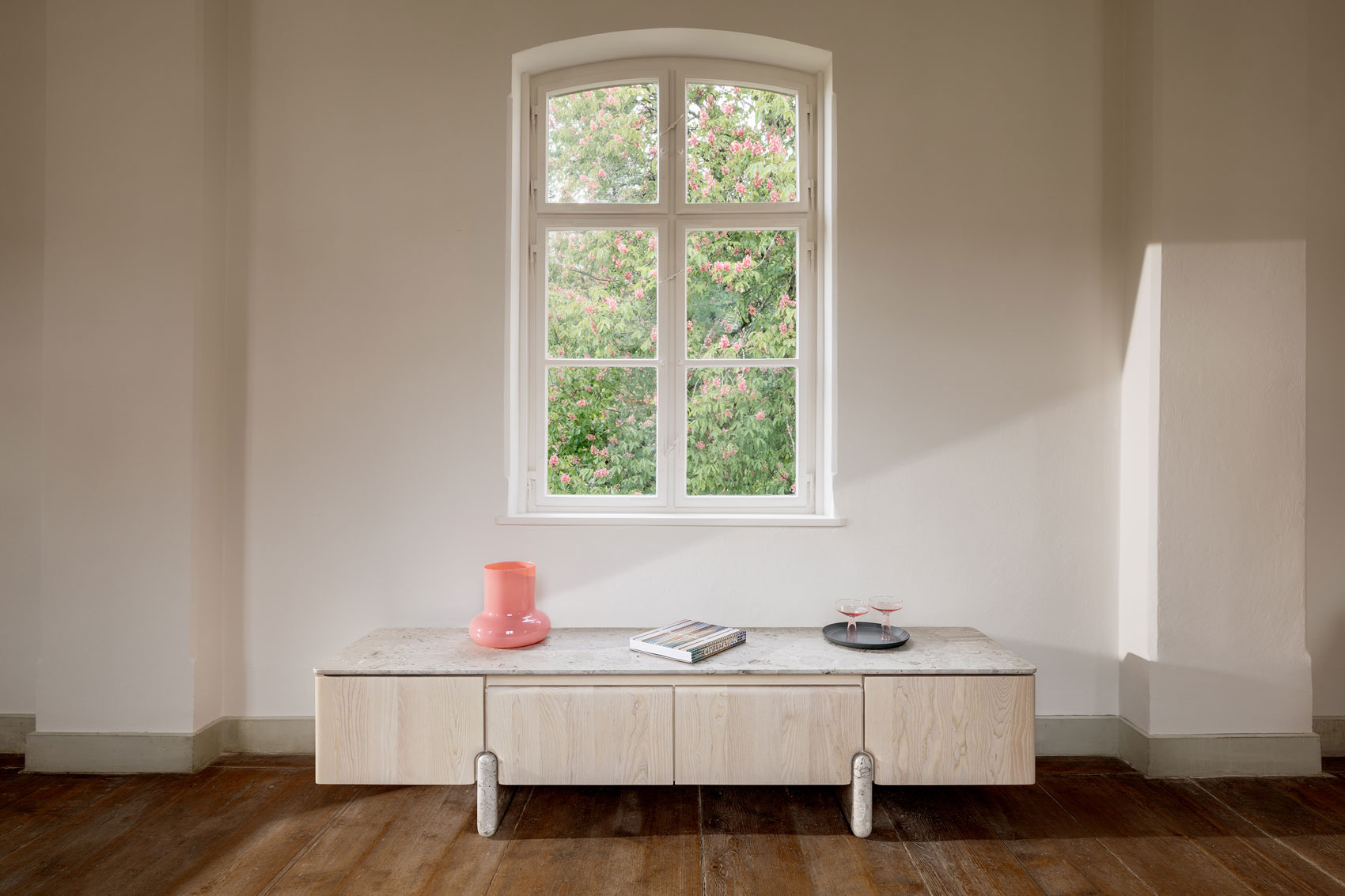 Frontansicht des Sideboards Onde von formstelle für Zeitraum in Esche mit Steinfüßen und Marmor Platte vor Fenster im Kloster Beuerberg.