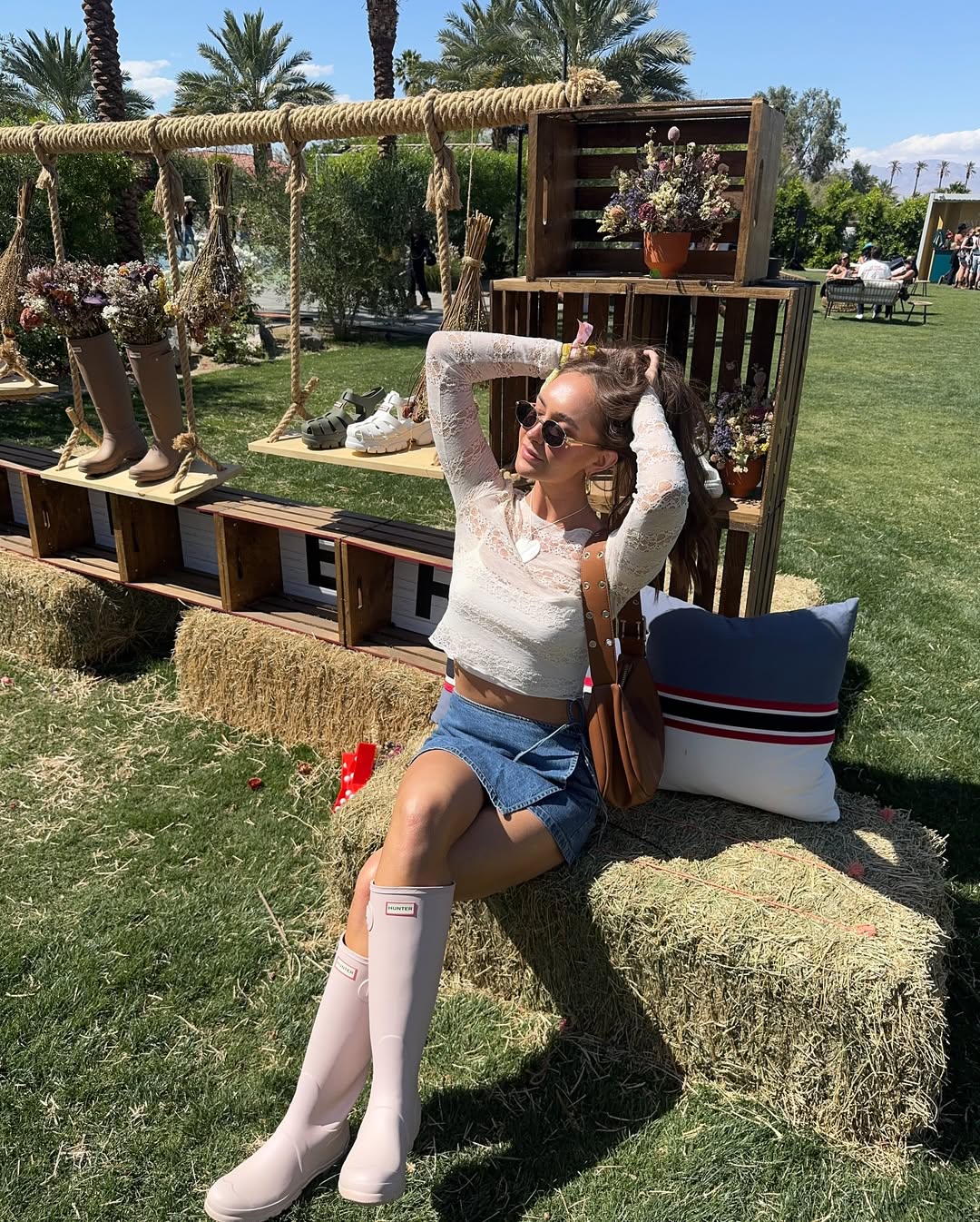 Woman in white lace top, denim shorts, and pink Hunter boots sitting on hay bale. Brought to you by Plural, NYC: Experts in Social Media Marketing Strategy and High-Quality Content Production.