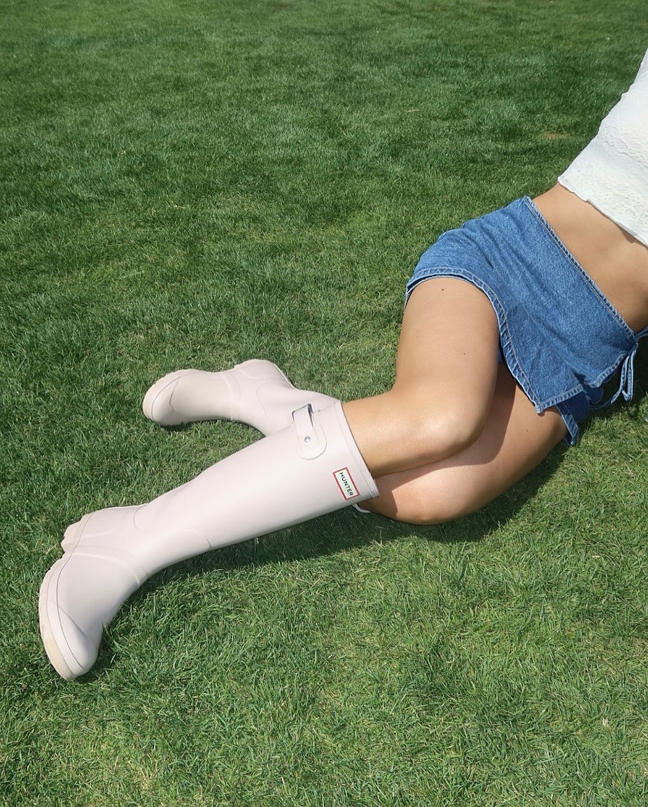 Pink Hunter rain boots with denim shorts on grass. Brought to you by Plural, NYC: Experts in Social Media Marketing Strategy and High-Quality Content Production.