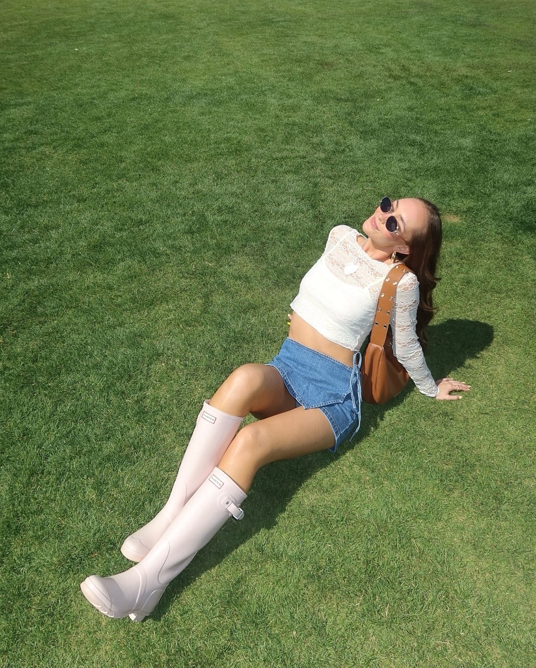 Woman in white lace top and pink Hunter boots relaxing on grass. Brought to you by Plural, NYC: Experts in Social Media Marketing Strategy and High-Quality Content Production.