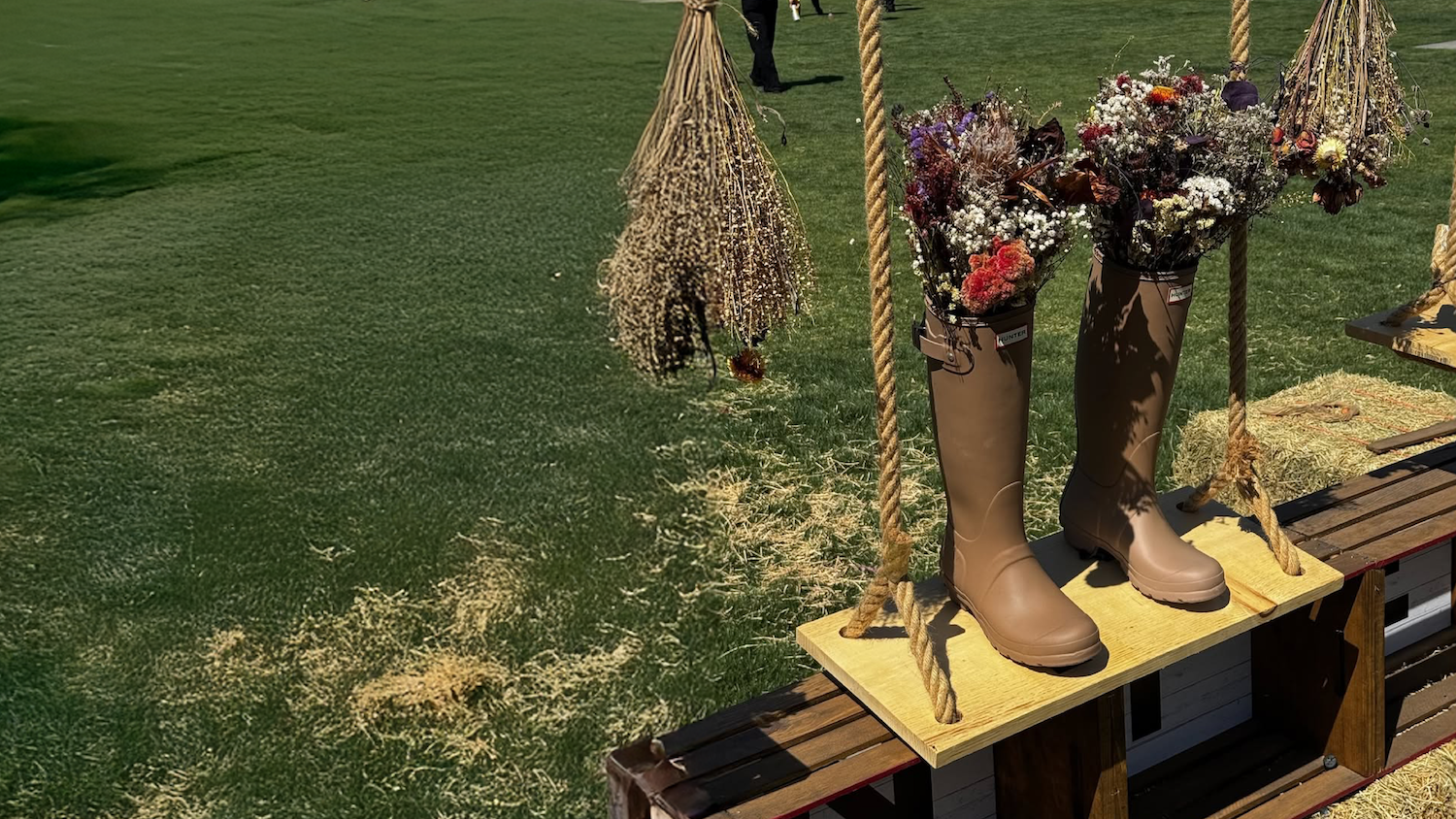 Tan rain boots filled with dried flowers suspended by rope on wooden swing with hay bales. Brought to you by Plural, NYC: Experts in Social Media Marketing Strategy and High-Quality Content Production.