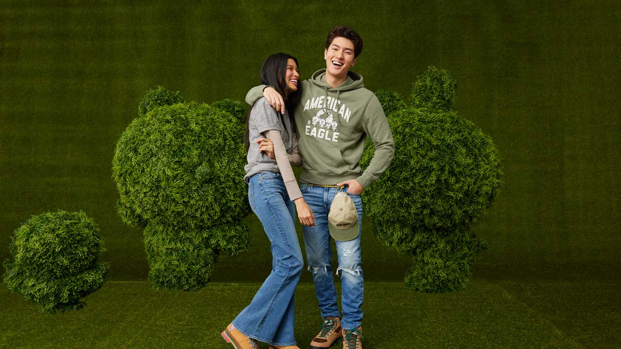  Two American Eagle models in casual wear posing against a green hedge. Brought to you by Plural, NYC: Experts in Social Media Marketing Strategy and High-Quality Content Production.