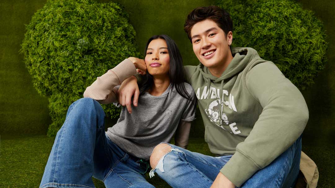  Two American Eagle models in casual wear posing against a green hedge. Brought to you by Plural, NYC: Experts in Social Media Marketing Strategy and High-Quality Content Production.
