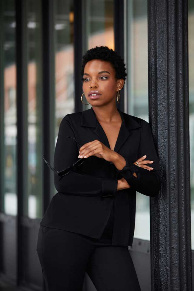 Model wearing a black Donna Karan power suit with gold jewelry. Brought to you by Plural, NYC: Experts in Social Media Marketing Strategy and High-Quality Content Production.