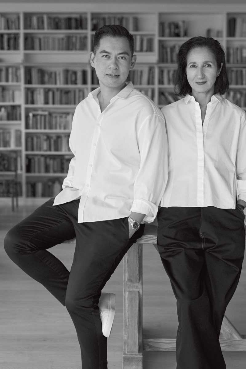 Black-and-white photo of a man and woman standing in front of a bookshelf, both wearing white shirts and dark pants, in a casual pose.