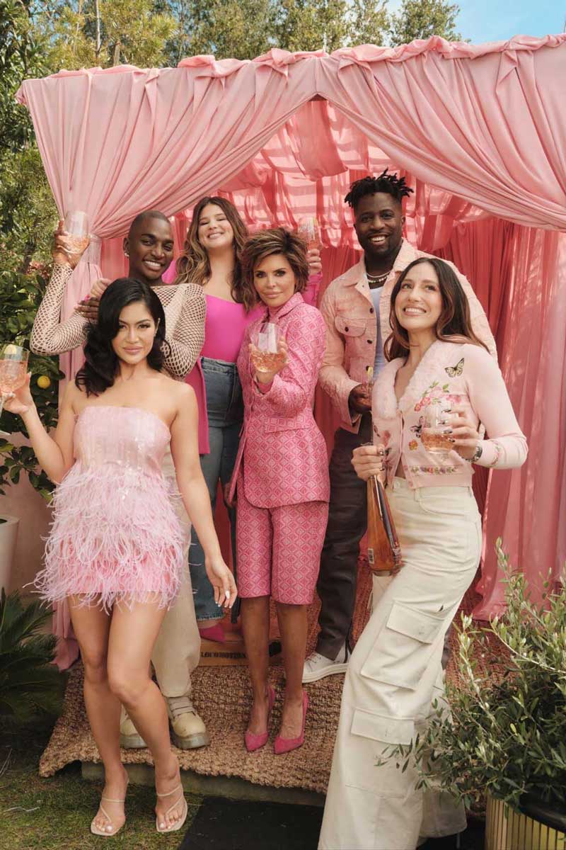 Group of six diverse people smiling and holding glasses of Don Julio rosado under a pink fabric canopy outdoors.