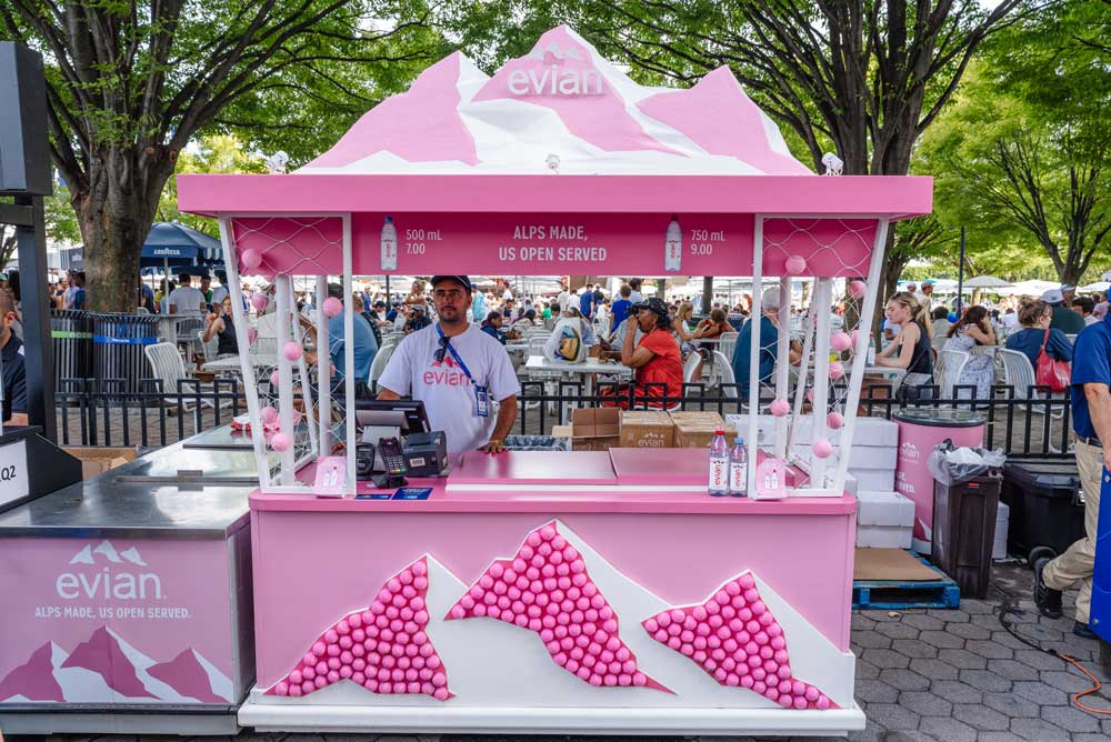 Pink Evian booth with mountain design selling water at an outdoor event with a vendor standing inside.