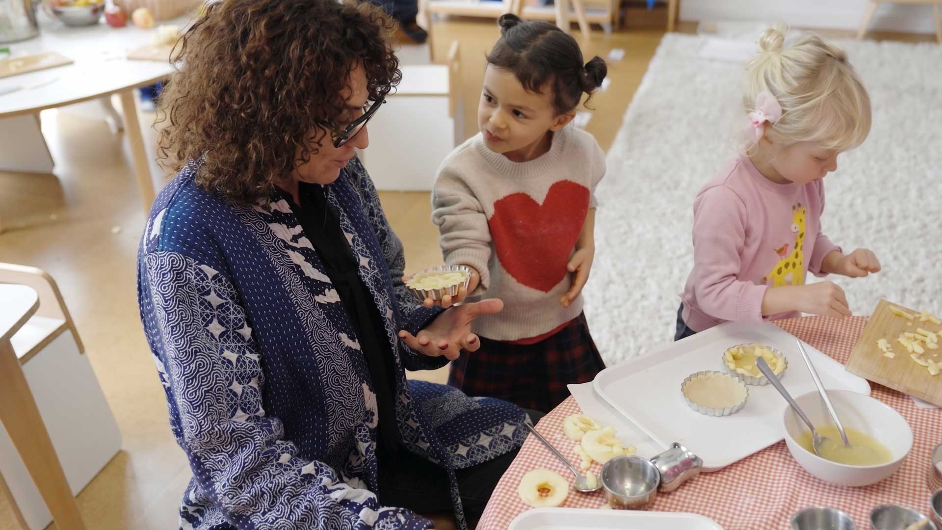Woman and two young girls preparing mini tarts with apple slices at a table.