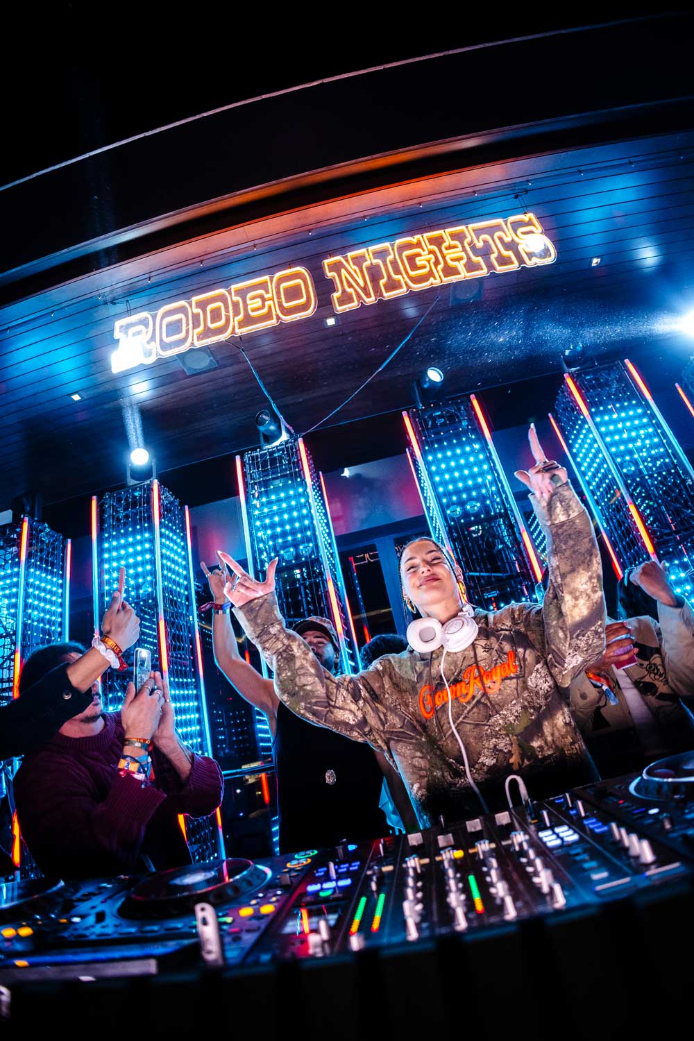DJ wearing headphones and Crown Royal hoodie performing at a vibrant Rodeo Nights event with colorful lights.