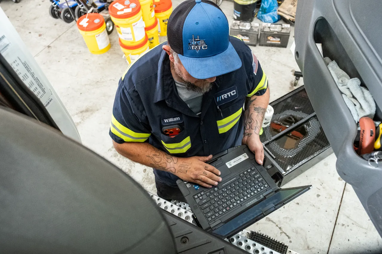 Truck diagnostics with a technician using a laptop to troubleshoot a commercial truck inside a repair shop.