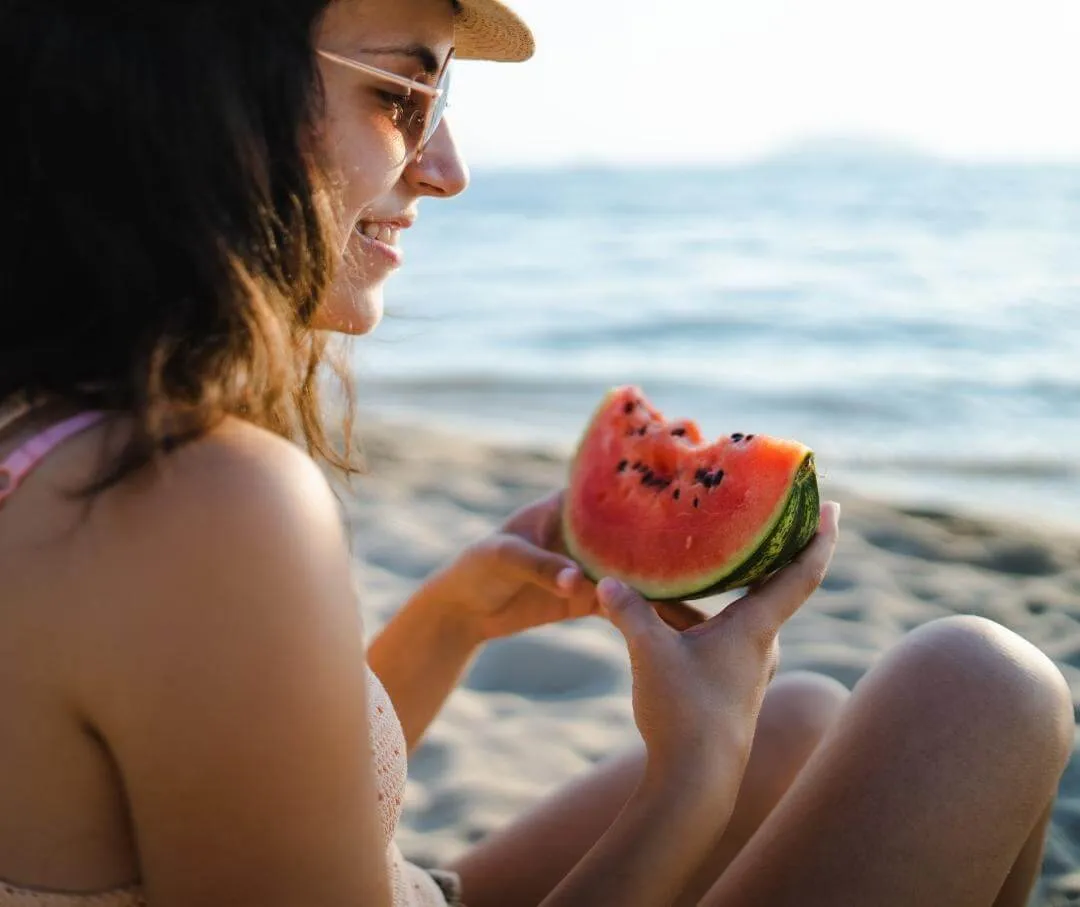 woman sitting on the beach eating watermelon with seeds