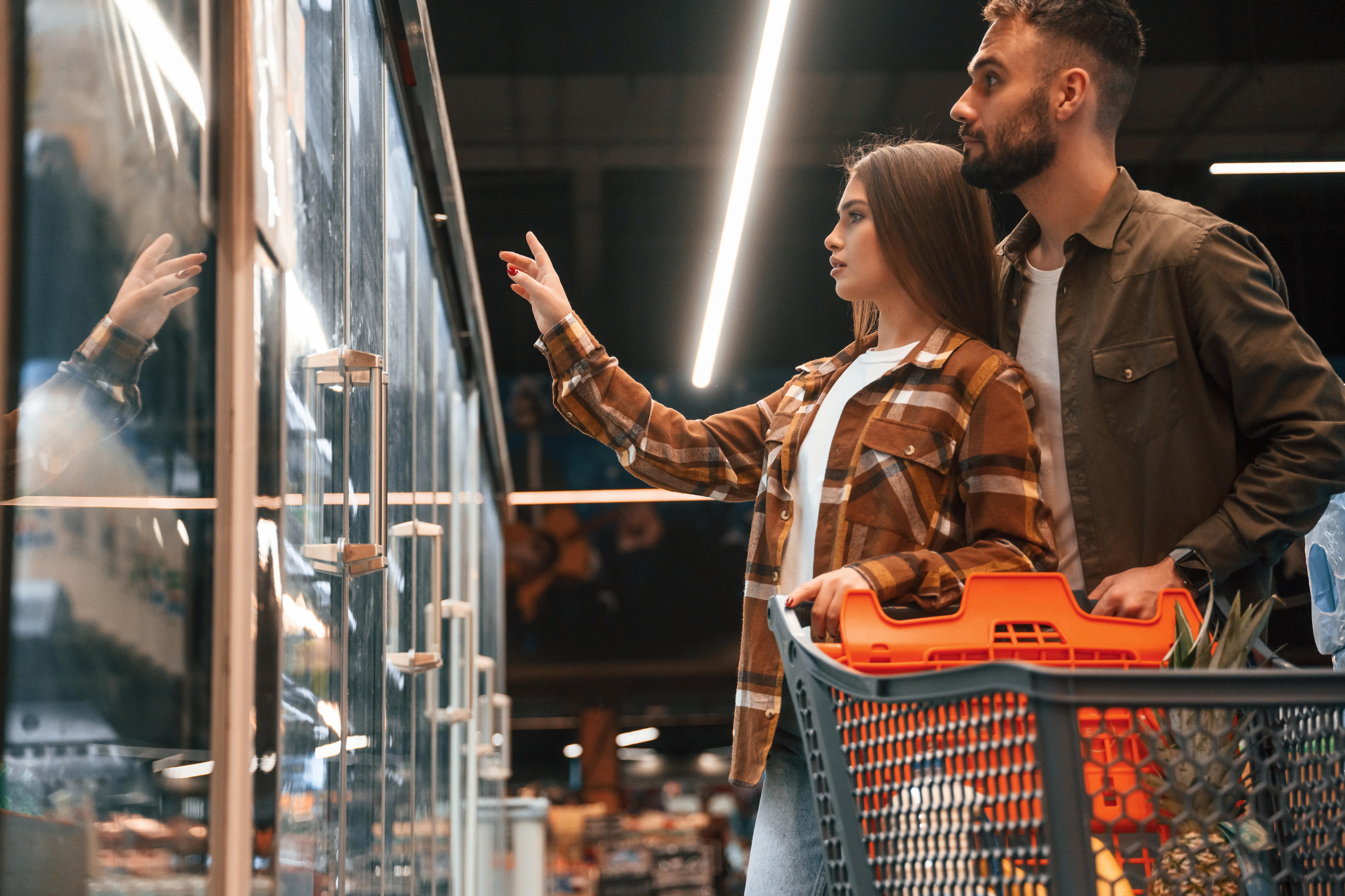 Couple shopping together, pointing at items in refrigerated grocery section